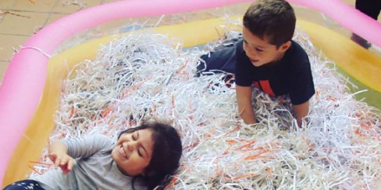 Infants jugant en una piscina de paper a la Ludoteca.